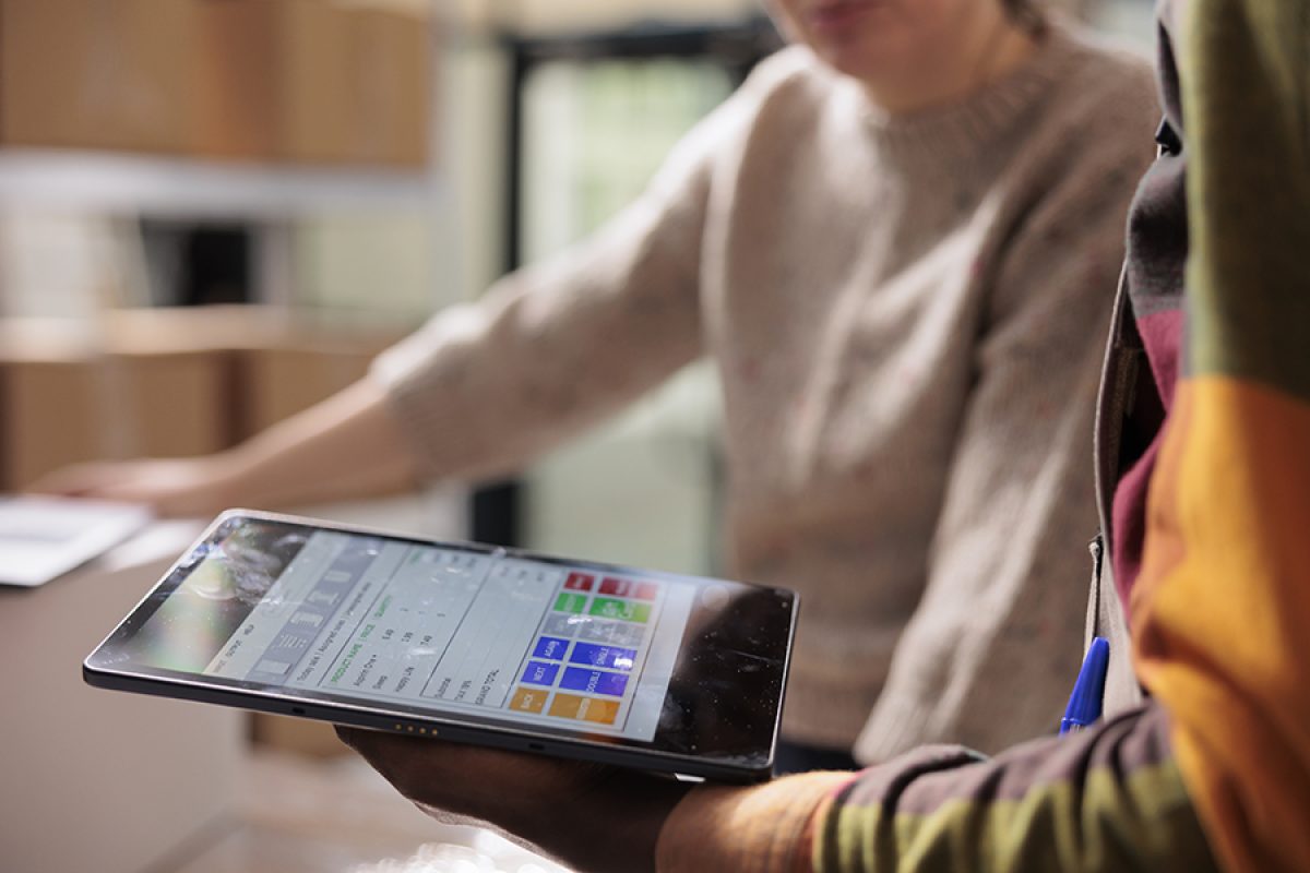 Stockroom workers analyzing online customers orders on digital device, preparing packages for shipping. Diverse employees working at merchandise logistics in warehouse. Close up shot